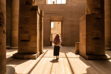 Traveler walking inside ancient Egyptian temple with sunlight and massive stone columns in Luxor